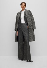 Cappotto in tweed bianco e nero sopra un completo coordinato con pantaloni a gamba larga. Camicia bianca fresca sotto, abbinata a calzature nere.