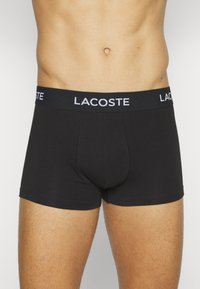 Čierne boxerky vyrobené z mäkkej tkaniny s širokým pásom s bielym logom "LACOSTE". Úzky strih s hladkou textúrou.