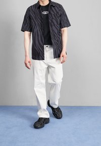 Kortärmad svart och grå zebrarandig skjorta över en svart t-shirt, kombinerad med vita byxor och svarta texturerade sneakers.