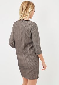 Vestido gris con mangas tres cuartos, que presenta un patrón texturizado y un escote negro. Silueta ligeramente ajustada, con un dobladillo a la altura de la rodilla.