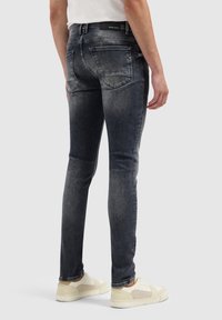 Slim-fit denim jeans in een vervaagde donkergrijze wassing, met twee achterzakken en minimalistische stiksels. Gecombineerd met lichtgekleurde sneakers.
