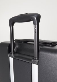 Black hard-shell suitcase with a retractable handle. Textured surface, silver accents, and dual wheels for mobility.