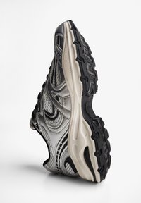 Chaussure de sport avec une tige en tissu maillé argent métallique et noir, détails texturés, semelle en caoutchouc avec bande de roulement et lignes d'accent contrastantes.