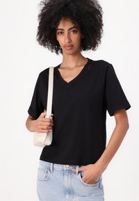 T-shirt nera a V con maniche corte, realizzata in un tessuto morbido. Abbinata a jeans azzurri chiari e a una piccola borsa crema.