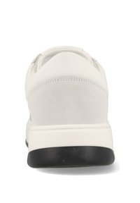 Zapatilla blanca con parte superior de cuero suave, detalles de ante en el talón, suela de goma negra y cordones elásticos para facilitar su uso.