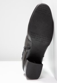 Botte en cuir noir avec semelle en caoutchouc affichant la marque "Anna Field" et la taille 37, avec une fermeture éclair latérale et un talon bloc.