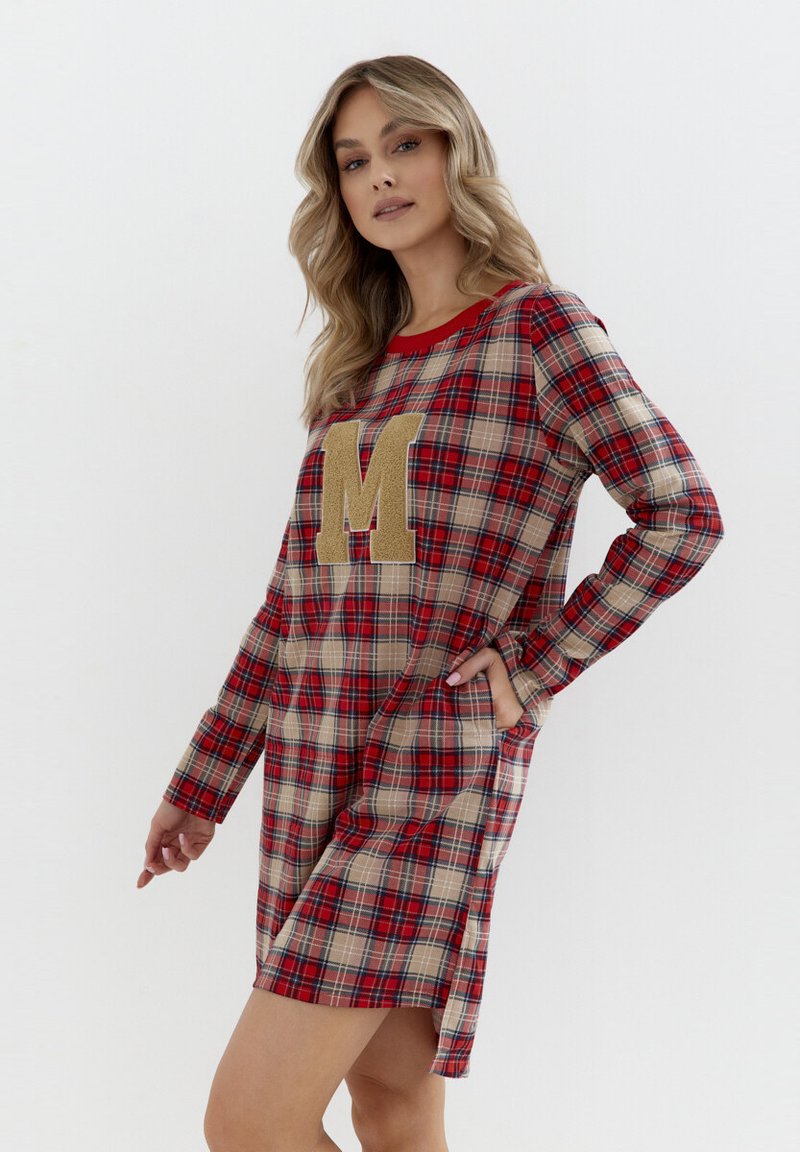 Czerwona i beżowa sukienka w kratkę z długimi rękawami i okrągłym dekoltem. Posiada dużą złotą literę "M" z przodu oraz boczne kieszenie.