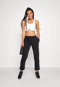 White sports bra with black logo, black sweatpants with pockets, and black sneakers. Model holds a black water bottle. Simple, athletic design.