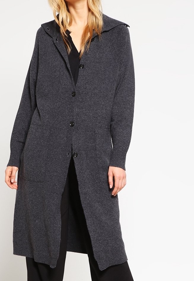 Cardigan long gris foncé boutonné avec poches, porté sur des vêtements noirs, présenté sur une personne de la nuque jusqu'au milieu des cuisses.