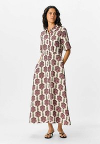 Robe chemise à imprimé floral en crème avec des roses roses et des feuilles vertes, dotée de manches courtes, d'une fermeture à boutons à l'avant et de poches sur les côtés.