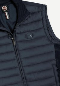 Námornícky prešívaný vest s predným zipsom, rebrovaným golierom a logom. Má prešívanú štruktúru a elegantný dizajn.