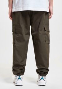 Cargo broeken in olijfgroen, met elastische boorden, zijzakken en een losse pasvorm. Gecombineerd met witte sneakers met turquoise accenten.