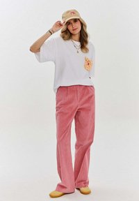 Bílý oversized tričko s kostkovanou kapsou, růžové manšestrové kalhoty, béžová kšiltovka a žluté boty. Jednoduchý design s uvolněným střihem.