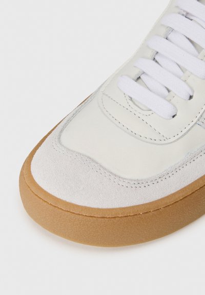 Vita lädersneakers med mockadetaljer, rund tå, vita snören och tanfärgad gummisula. Har sömmar längs kanterna.