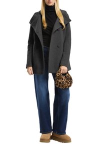 Grijze wolblend jas met een brede kraag en dubbelzijdige knopen, gedragen over een zwarte turtleneck en gecombineerd met blauwe jeans en een handtas met luipaardprint.