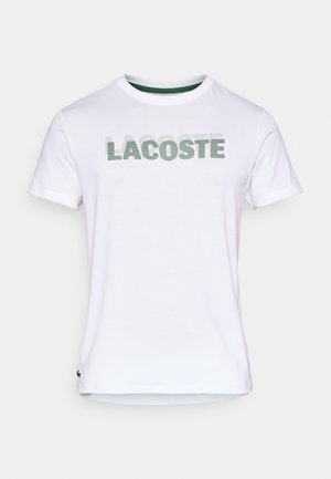 Witte katoenen T-shirt met groene "LACOSTE" opdruk. Ronde halslijn met contrasterende groene bies. Korte mouwen. Regular fit.