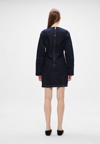 Μπλε τζην φόρεμα με μακριά μανίκια, σκούρο μπλε χρώμα, ορατές ραφές και κλείσιμο με φερμουάρ στην πλάτη. Μήκος έως το μεσαίο μηρό, με δομημένη εφαρμογή.