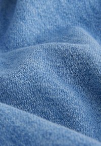Tela de mezclilla azul con una superficie texturizada, que presenta un tejido apretado y variaciones sutiles en el tono, creando una apariencia suave y lisa.