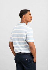 Polo shirt à rayures bleu clair avec des manches courtes, accompagné d'un pantalon bleu marine foncé avec une ceinture tressée et des détails d'accent subtils.