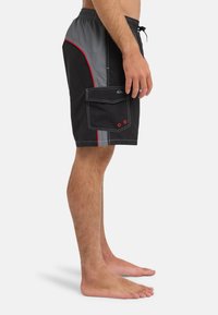 Μαύρα μαγιό σορτς με γκρι λεπτομέρειες, κόκκινη περιέλιξη και πλαϊνή τσέπη cargo. Κατασκευασμένα από ελαφρύ υλικό, διαθέτουν ελαστική μέση και κορδόνι.