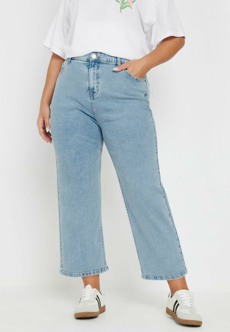 Jeans de mezclilla de pernera ancha en azul claro con una cintura alta, que cuentan con bolsillos frontales y un dobladillo limpio. Combinados con zapatillas blancas.