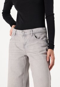 Lys grå straight-leg jeans laget av denim, med frontlommer, knappelukking og lett slitasje for tekstur.