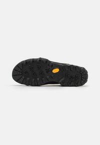 Czarna gumowa podeszwa z głębokim bieżnikiem dla lepszej przyczepności, z logo Vibram w kolorze żółtym. Nowoczesny, surowy i teksturowany design.