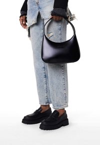 Sort læderhåndtaske med et buet håndtag, båret med lyseblå slidte jeans og sorte chunky loafers med tyk sål.