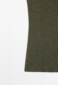 Gros plan sur la partie inférieure d’un tissu tricoté vert olive avec un bord incurvé subtil sur fond blanc.