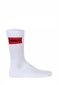 Weiße Baumwollsocke mit gerippter Textur, die ein rotes rechteckiges Logo zeigt, auf dem das Wort "HUGO" in Schwarz auf der Außenseite gestickt ist.