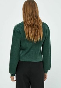 Maglione a coste verde con maniche lunghe e design corto. Presenta un tessuto testurizzato e un collo tondo, senza chiusure visibili.