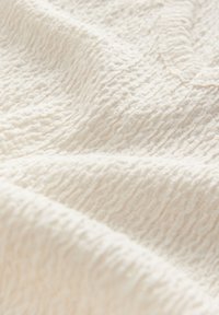 Textured cream fabric with a wavy pattern, featuring a soft, slightly crinkled surface, ideal for a cozy look and feel.