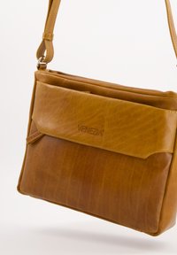 Brown leather handbag with a smooth texture, featuring a front flap and logo detail. Includes an adjustable strap for versatility.