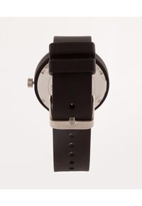Black silicone watch with a round case, silver hardware, and buckle closure. Features textured band and visible time markers on the face.