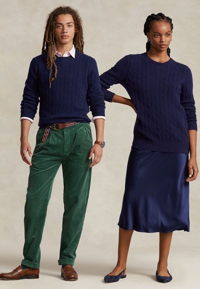 Δεξιά μπλε πουλόβερ με πλέξη καλωδιού, πράσινο παντελόνι από κορδόνι, καφέ παπούτσια. Δεξιά εμφανίζει μπλε σατέν φόρεμα με λεπτές τιράντες και αντιστοιχισμένα μπλε φλατ παπούτσια.