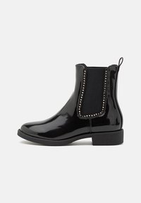 Bottines chelsea en cuir verni noir avec des panneaux élastiques sur les côtés, ornées de clous métalliques, dotées d'un petit talon carré et d'une languette d'enfilage.