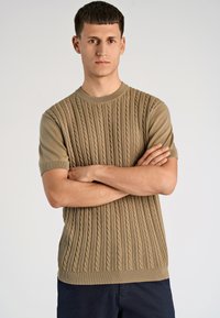 Μπεζ πλεκτό πουλόβερ με κοντά μανίκια, διακοσμημένο με υφασμάτινη σχεδίαση καλωδίωσης, λαιμόκοψη ριμπ και ίσια ραφή στο κάτω μέρος.