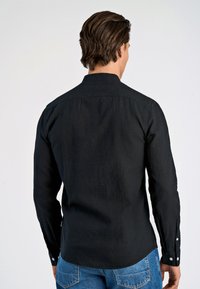 Camisetta nera a maniche lunghe con colletto, tessuto testurizzato e dettagli con bottoni sui polsini. Indossata con jeans di denim blu.