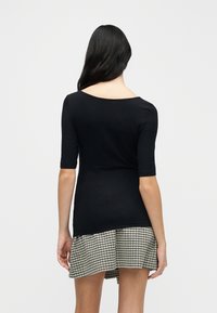 Μαύρο εφαρμοστό τοπ με κοντά μανίκια, διαθέτει λαιμόκοψη σε σχήμα scoop. Συνδυασμένο με φούστα ασπρόμαυρου μοτίβου houndstooth με βολάν στο τελείωμα.