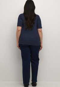 Camisa de manga corta azul marino, combinada con jeans rectos de color azul oscuro. Tejido suave con un ajuste relajado, mostrado desde la vista trasera.