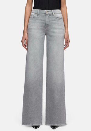 Kvinde iført grå højtaljede, vidde bukser i denim kombineret med en sort ærmeløs top og sorte spidse sko.