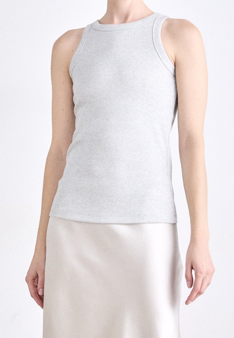 Personne portant un débardeur gris clair côtelé ajusté et une jupe en satin lisse de couleur claire, sur un fond uni.