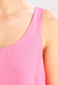 Top sin mangas de color rosa, confeccionado con una tela suave y ligera, con un escote redondeado que deja al descubierto la piel en el hombro y la parte superior del pecho.
