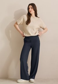 Beige trui met korte mouwen, gecombineerd met marineblauwe wijde broek, met een gladde textuur en subtiele stiksels, voltooid met witte sneakers.