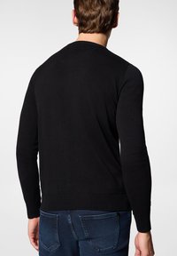 Czarny sweter z okrągłym dekoltem, z długimi rękawami, z ribbowanym wykończeniem mankietów i dołu, o gładkiej teksturze dzianiny. Nosi się go na niebieskie dżinsy.