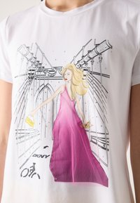 White T-shirt featuring a graphic of a woman in a pink dress, holding a yellow DKNY bag, with bridge and bike lane illustrations.