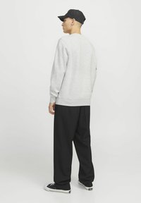 Un sweat-shirt gris à col rond avec des poignets côtelés, associé à un pantalon noir ample et des baskets noires, vu de dos.