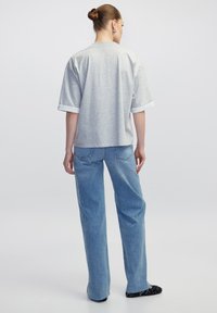 Grijze oversized t-shirt met korte witte mouwen, gecombineerd met lichtblauwe high-waisted denim jeans. Het bovenstuk heeft een relaxte pasvorm en een casual ontwerp.