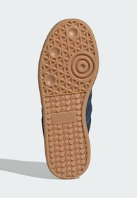 Suola di sneaker in gomma color tan con un motivo di presa texturizzato e accenti circolari. Presenta un logo del marchio in rilievo al centro.