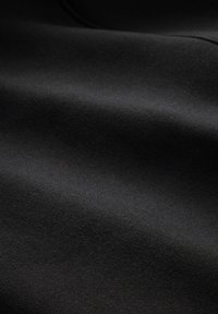 Tessuto nero con una texture liscia e opaca e sottili variazioni sulla superficie. Le pieghe curve creano profondità e dimensione.